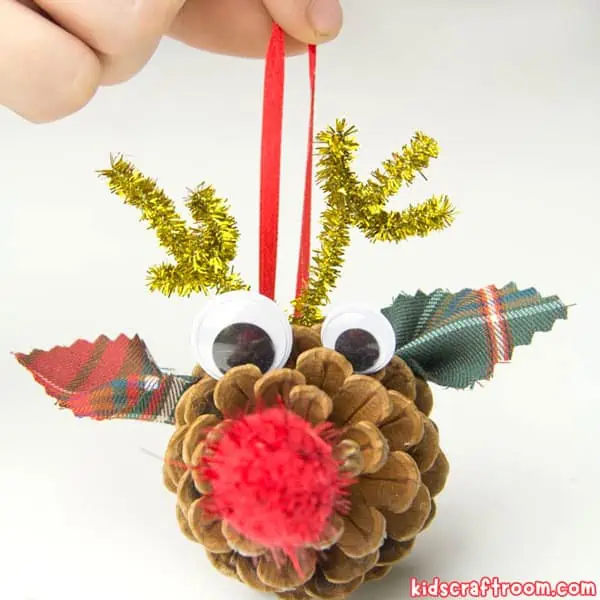 A hand holding a pinecone reindeer Christmas ornament.