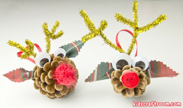 Two pinecone reindeer ornaments side by side. The heads are made with pinecones. Fabric ears and pipe cleaner antlers have been stuck on. They have a pom pom nose.