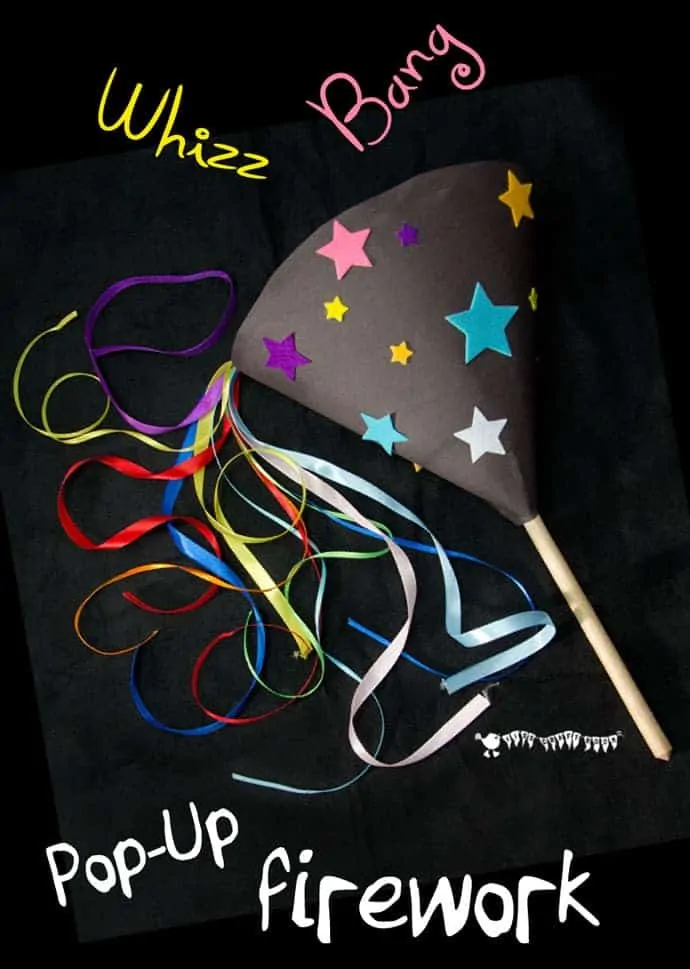 A homemade firework toy lying on a black surface. The firework is decorated with colourful stars and has ribbon fireworks popping out.
