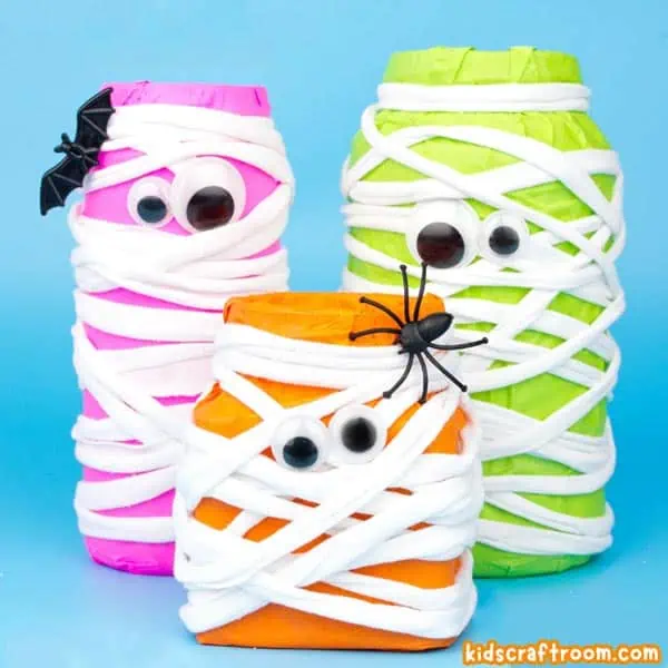 A close up of three Neon Mason Jar Mummies. One pink, one orange and one green. They've been made by covering jars in brightly coloured tissue paper and then wrapping them in white tshirt yarn.