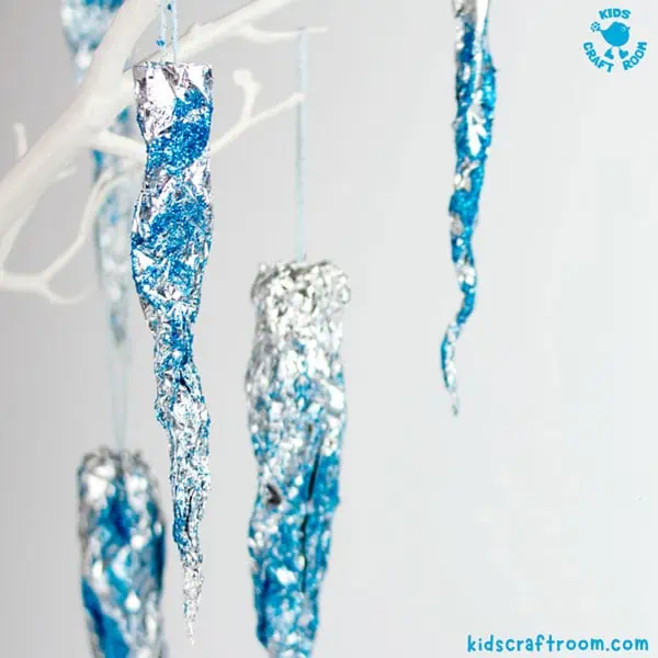 A close up of a selection of Sparkly Icicles hanging from white tree branches. They are made of silver foil and are sprinkled with blue glitter.