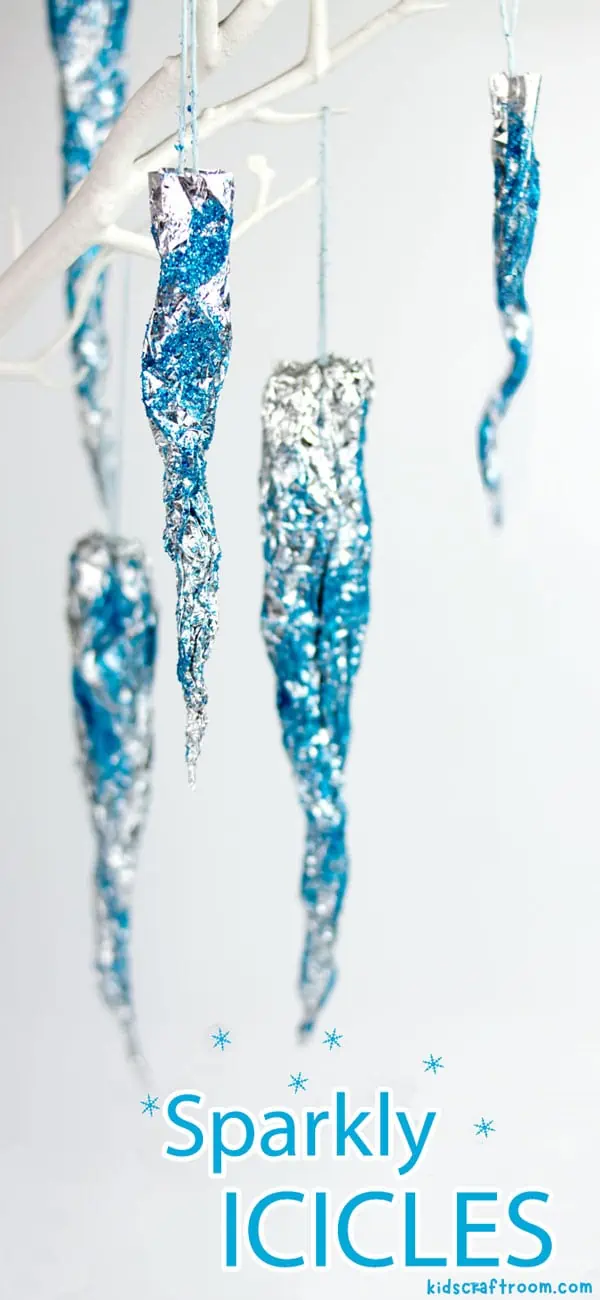 A selection of Sparkly Icicles hanging from white tree branches. They are made of silver foil and are sprinkled with blue glitter.