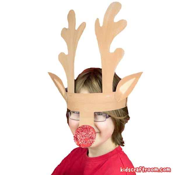 A brown haired child wearing a paper reindeer antler headband. It has a large red sparkly glitter nose.