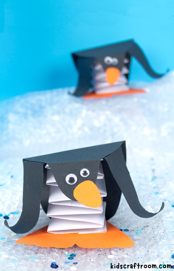 Two paper pop up penguin crafts standing on sloping ice. You can see the paper concertina folded tummy spring.