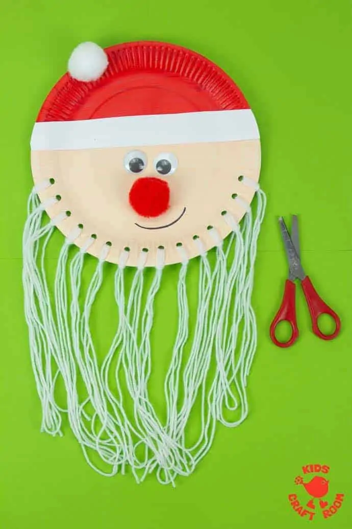 Trim The Beard Paper Plate Santa Craft lying on a green background. His yarn beard is very long, ready to be cut.