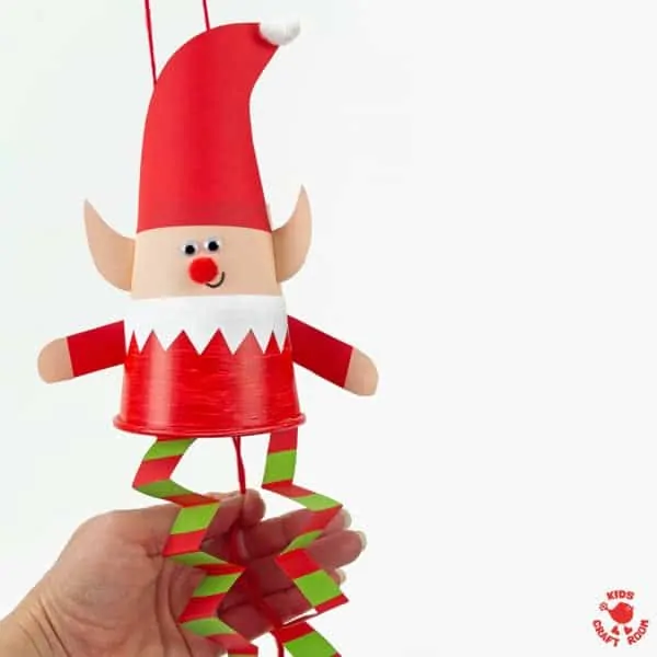 A paper cup elf with a hand showing you where to pull the strings to make it jump.