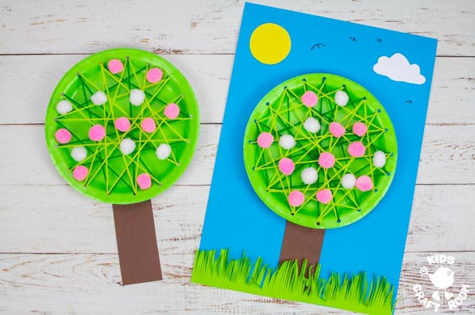  Two finished paper plate blossom tree crafts lying side by side. The one on the right is mounted on blue paper.