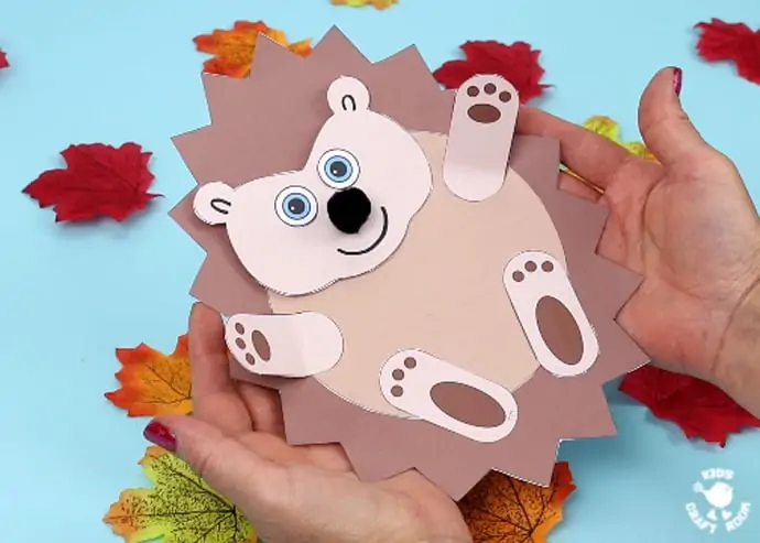 Moving Baby Hedgehog Craft lying in open hands with a background of leaves.