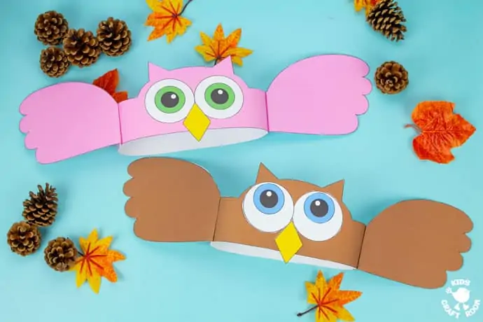 Owl Hat Craft in pink and brown on a blue tabletop with pinecones and leaves scattered around them.