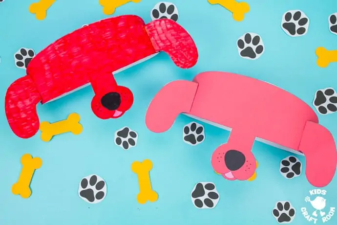 Landscape image of two Clifford The Big Red Dog Hats lying face up, side by side on a blue table top. They are surrounded by paper dog footprints and yellow bones.