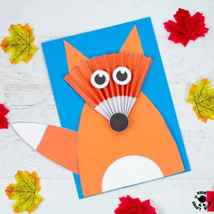 A square image of a Paper Fan Fox Craft lying on table surrounded by autumn leaves. 