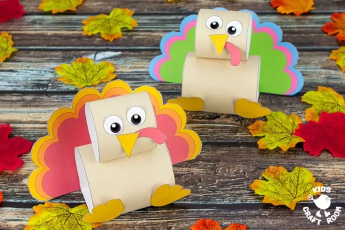 Two pop up turkey crafts, one in front of the other, on a wooden table top scattered with autumn leaves. 