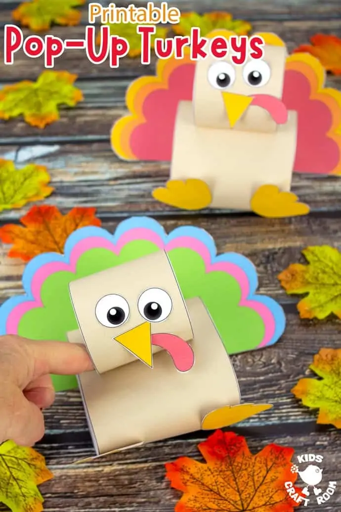 Two pop up turkey crafts on a wooden table top scattered with autumn leaves. A finger is pushing the front turkey down.