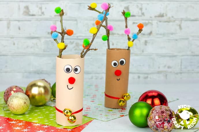 2 Cardboard Tube Reindeer Crafts standing on a table surrounded by Christmas wrapping paper and baubles.