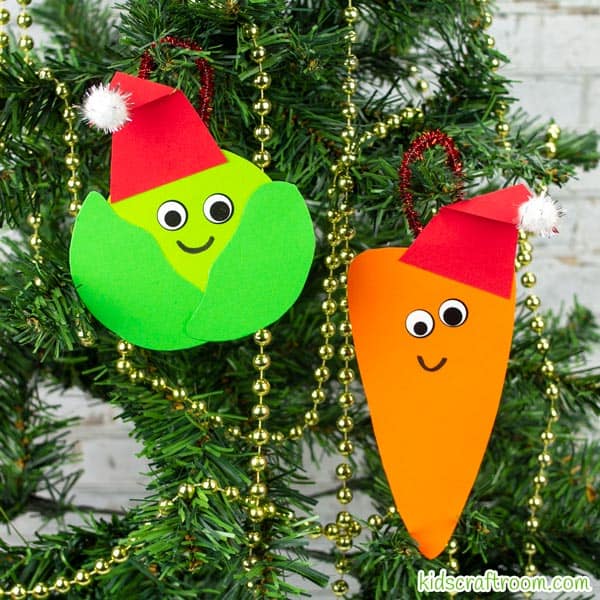 A Brussels sprout and carrot Christmas ornament hanging side by side on a Christmas tree.