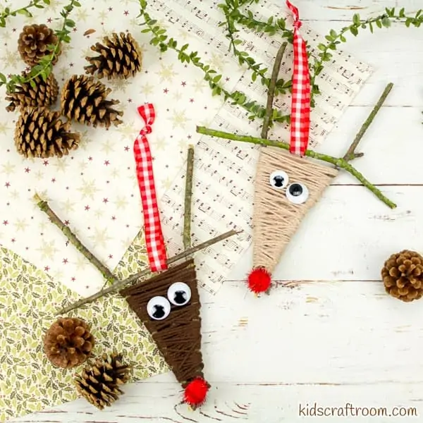 2 Yarn Wrapped Reindeer lying on a table top strewn with Christmas wrapping paper and pine cones.