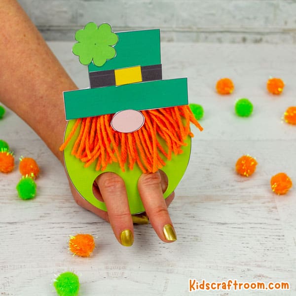 Leprechaun Gnome Finger Puppet being played with on white table with orange and green pompoms scattered around.