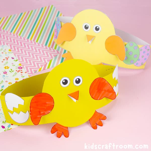 2 Easter chick hats on a pink tabletop. In the background there is a selection of pretty Easter papers.