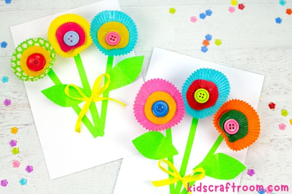 Two colourful bunches of Cupcake Liner Flowers lying side by side on a tabletop. Flower shaped buttons are scattered around them.