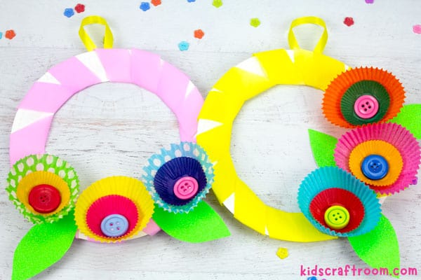 2 cupcake liner flower wreaths, one pink, one yellow, lying side by side on a white wood tabletop.