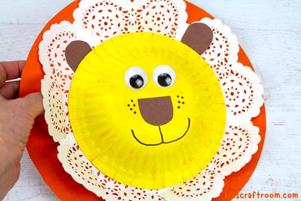 An orange 3D doily lion craft being held in someone's hand. 