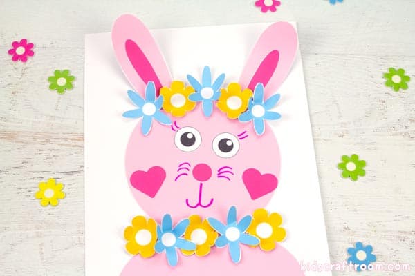 A pink Flower Power Bunny Craft on a white tabletop with scattered flowers around it. 