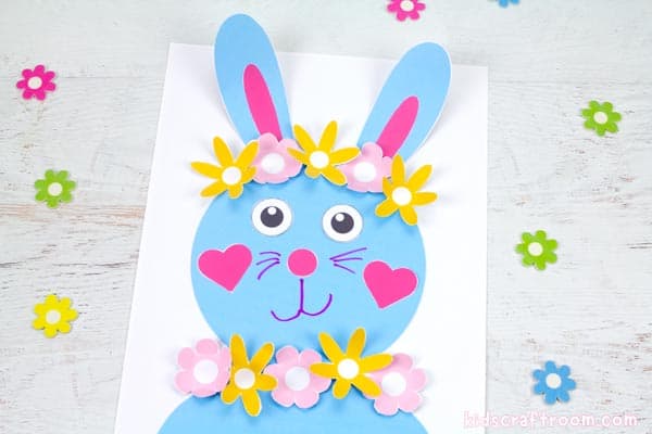 A blue Flower Power Bunny Craft on a white tabletop with scattered flowers around it. 