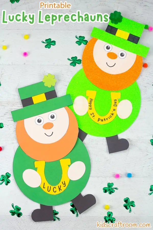 2 Lucky Leprechaun crafts lying on a white wood table top surrounded by scattered shamrock leaves and coloured pom poms.