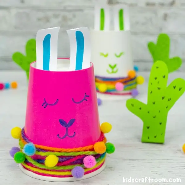 A pink paper cup llama craft next to a paper cactus.