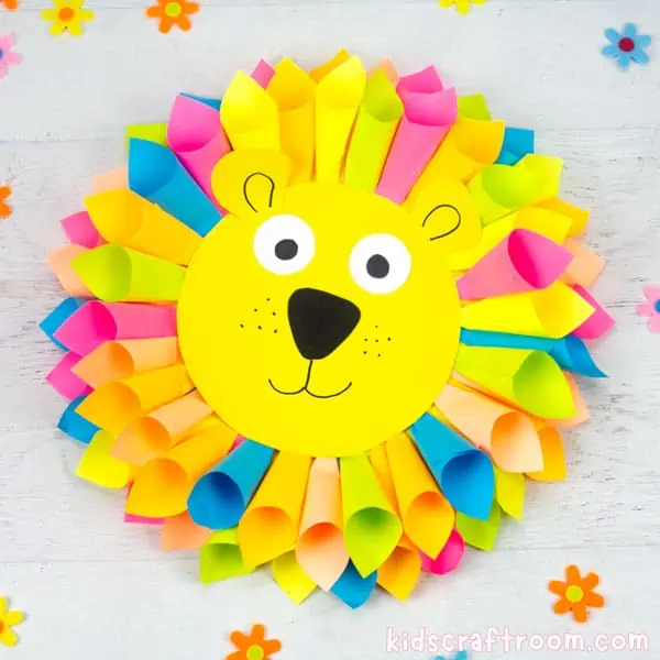 A lion head made from colourful rolled sticky notes for the mane. Lying on a table top surrounded by scattered paper flowers. 