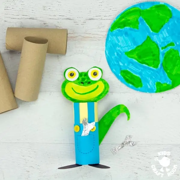 A gecko craft made from a cardboard tube lying on a white tabletop with a picture of the earth on the table next to it..
