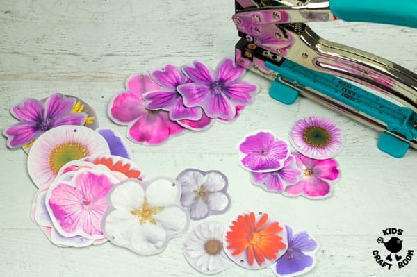 Shrink plastic flowers cut out lying on a table with a hole puncher.