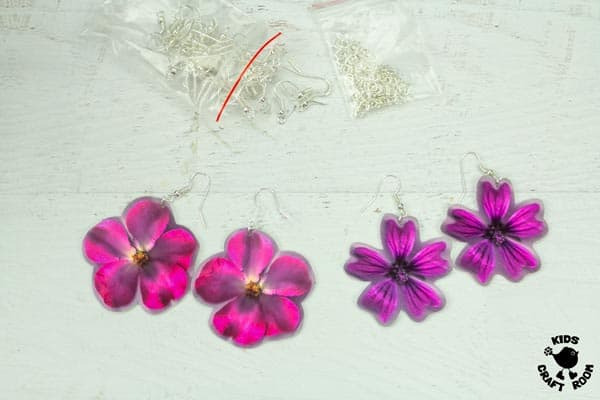 Pink shrink plastic flower earrings lying on a white tabletop.
