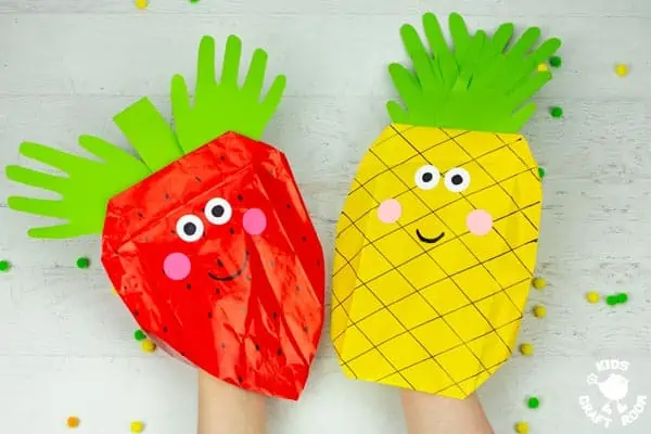 A strawberry and pineapple paper bag puppet being held next to each other.