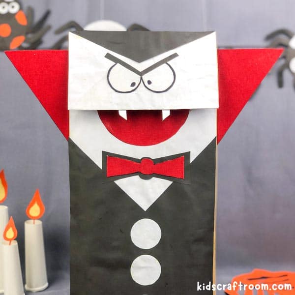 Paper Bag Vampire Puppet against a grey background. There are candles and paper spiders around him.