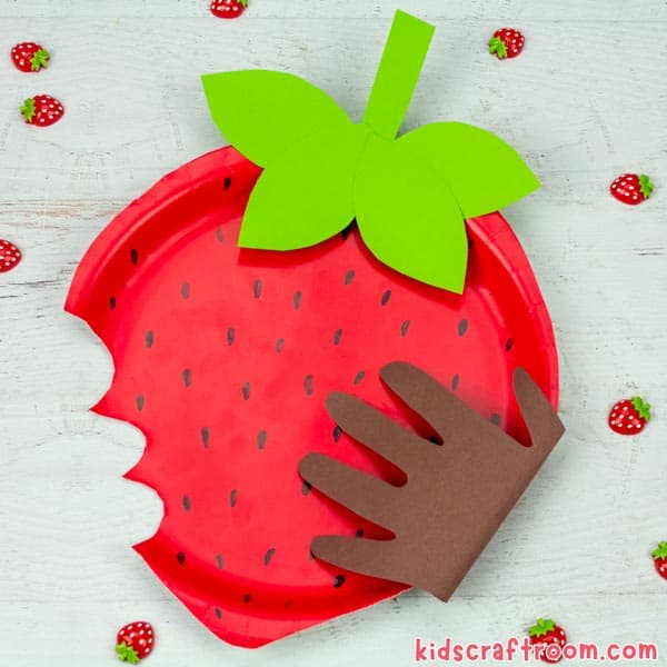 Paper Plate Strawberry Craft on a white table top surrounded by little strawberry ornaments.