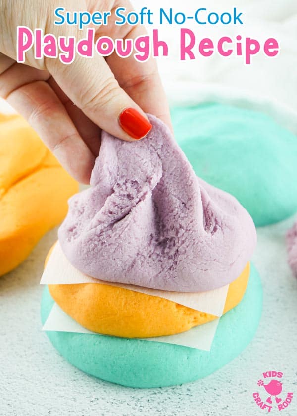 A pile of three colours of playdough. The top, purple colour is being stretched upwards by a hand wearing red nail polish.