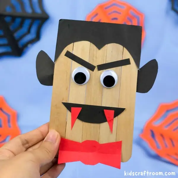 A hand holding a Popsicle Stick Vampire Craft against a background of blue.