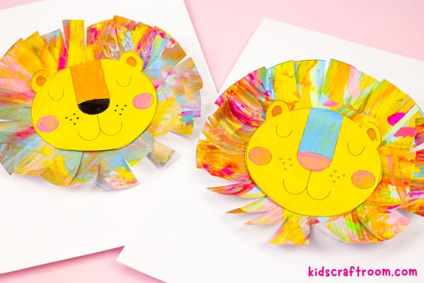 two finished lions lying on a pink tabletop, side by side. One has an orange nose and one has a blue nose.