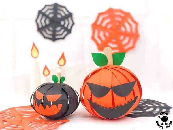 3D Paper Pumpkins on display on a tabletop. They are surrounded by candles and cobwebs.