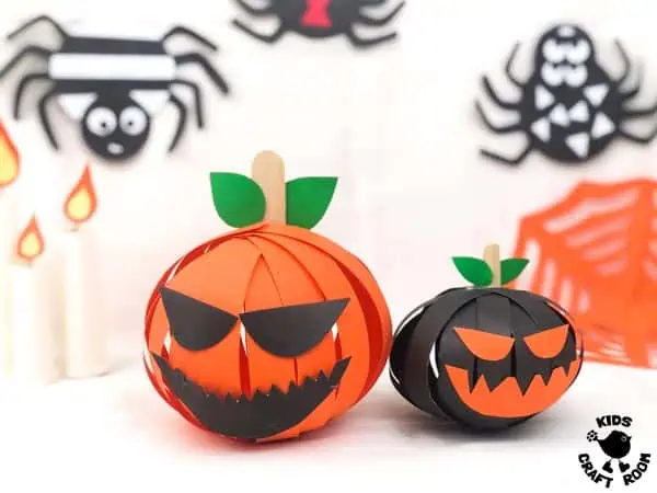 Two 3D Paper Pumpkin Crafts, one orange, one black sat on a white table top. Colourful paper spiders decorate the wall behind them.