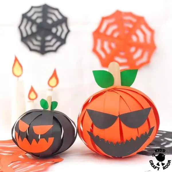 A small black and large orange 3D Paper Pumpkin on a white tabletop. Surrounded by candles and cobwebs.