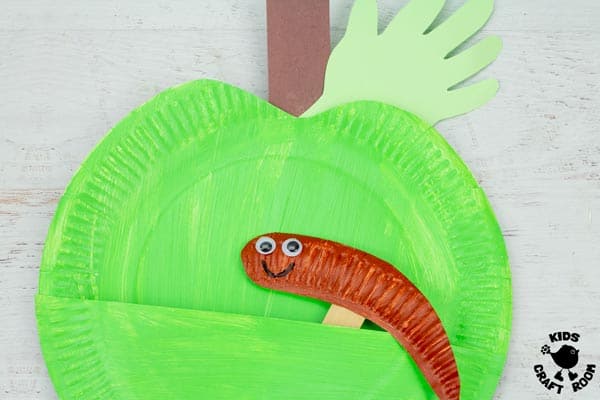 A green Paper Plate Apple Puppet Craft with a brown smiling worm.