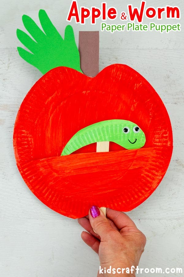 A Red Paper Plate Worm in Apple Puppet Craft being held in a hand. The green worm is poking out smiling. 