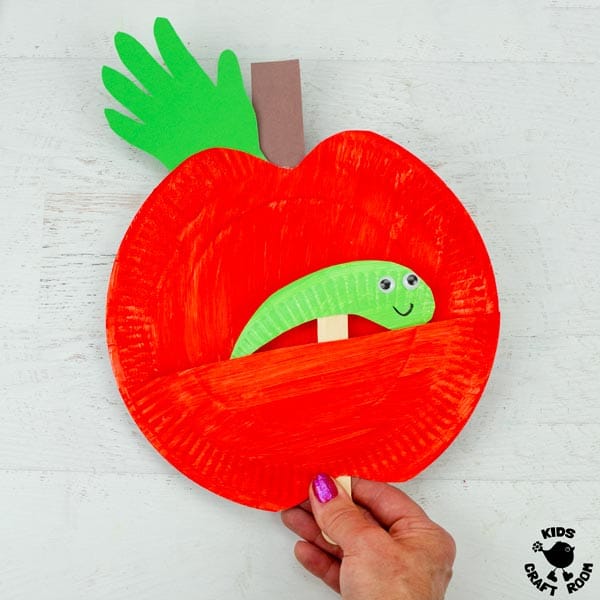 A red Paper Plate Worm in Apple Puppet being held in a woman's hand.