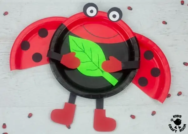A Paper Plate Ladybug Craft on a white tabletop surrounded by little wooden ladybug charms.