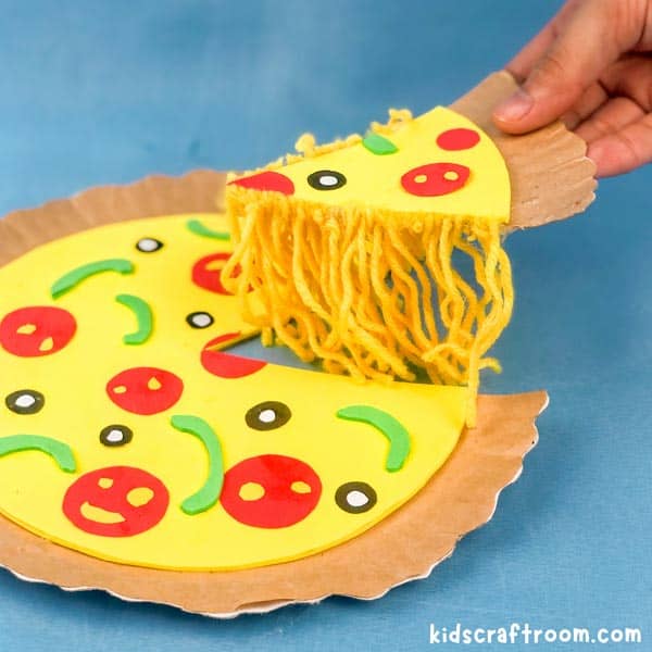 Paper Plate Pizza Craft on a blue backdrop. A hand is picking up a slice showing the melted cheese made from yarn.