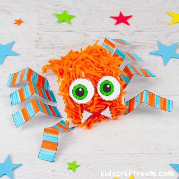 A square image of a printable hairy spider craft. It has an orange furry body and blue and orange striped legs.