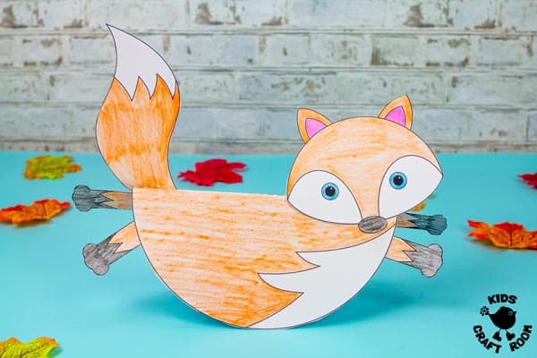 A rocking fox craft on a blue tabletop with scattered autumn leaves around it. The fox has been coloured in by a child.