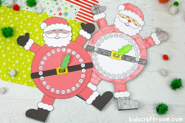 Two made Santa advent calendar clocks. They're lying on a table with Christmas gift wrap behind them and pom poms scattered around them.